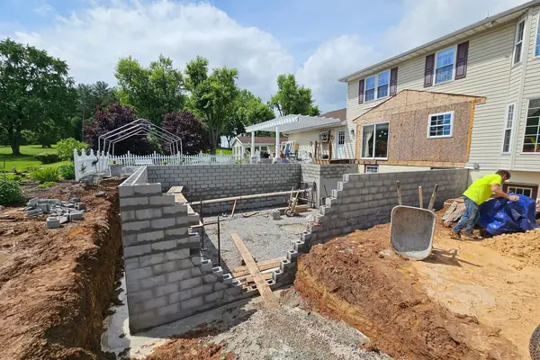 An excavated back yard with poured footers and block retaining walls going up behind a house.