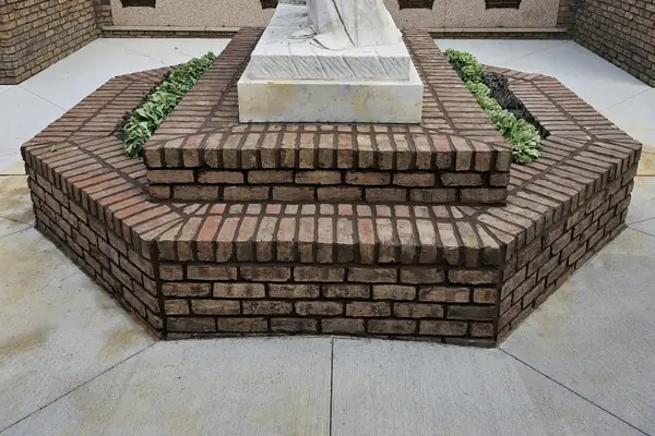 A hexagonal coursed brick base and steps built around a stone monument.