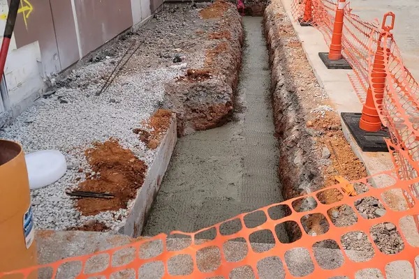A drainage trench cut and concreted alongside a commercial building, fenced off with cones.
