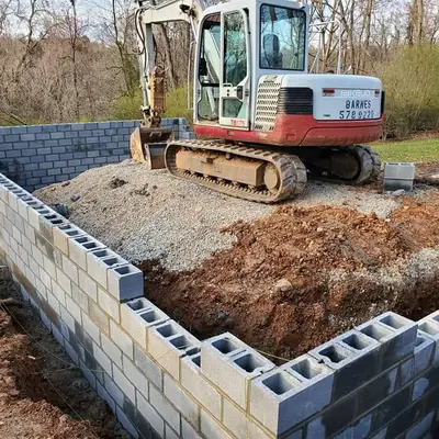 A block foundation wall with a mini excavator working behind it.