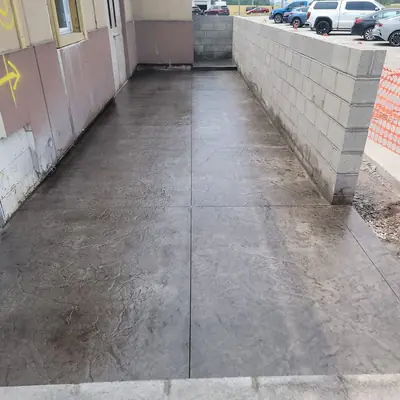 A finished stamped concrete service walkway beside a new block wall.