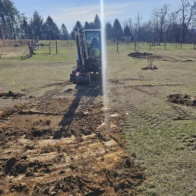 A mini excavator stripping a flagged septic area in an open field.