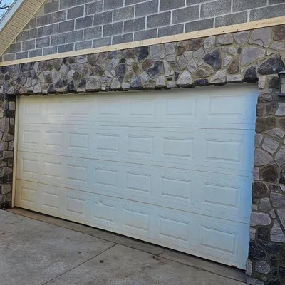 A garage front faced in stacked stone veneer around the door opening.